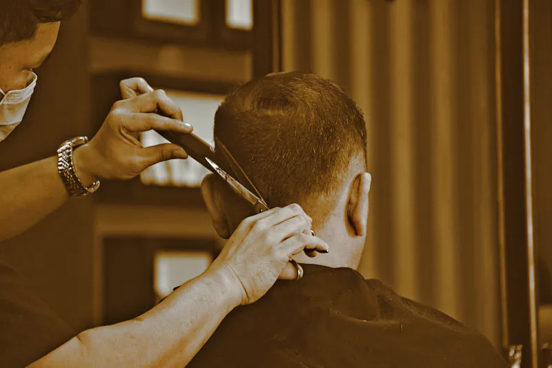 A barber taking scissors to the back of a client’s head in a dark shop