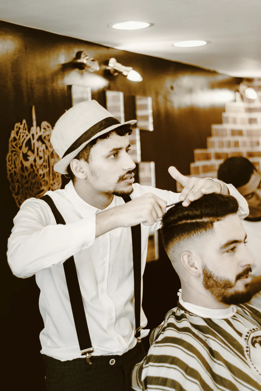 A barber in a straw hat and braces combing a client’s fade into shape