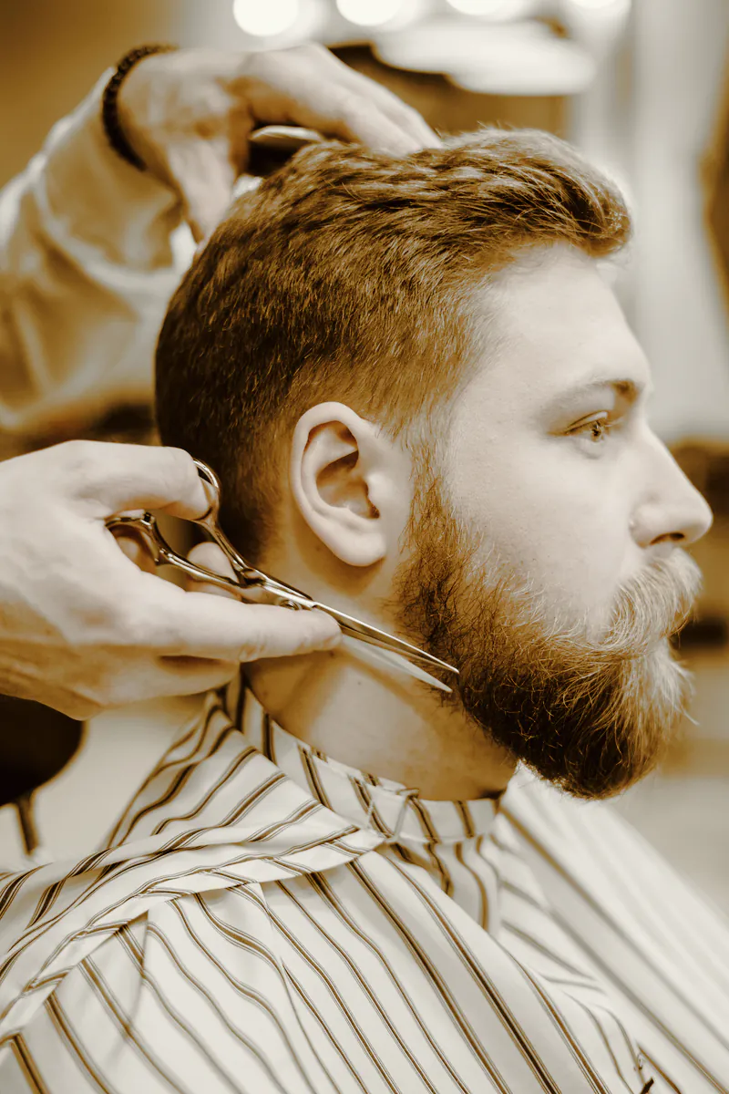 A barber shaping a client’s beard line with scissors
