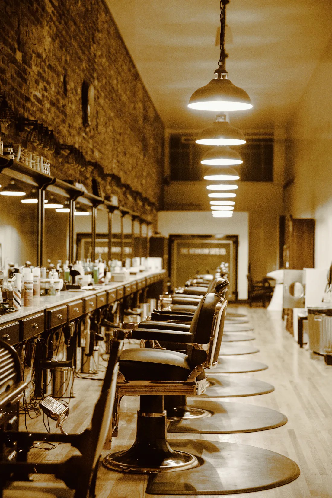 A long row of barber chairs and mirrors under hanging pendant lights