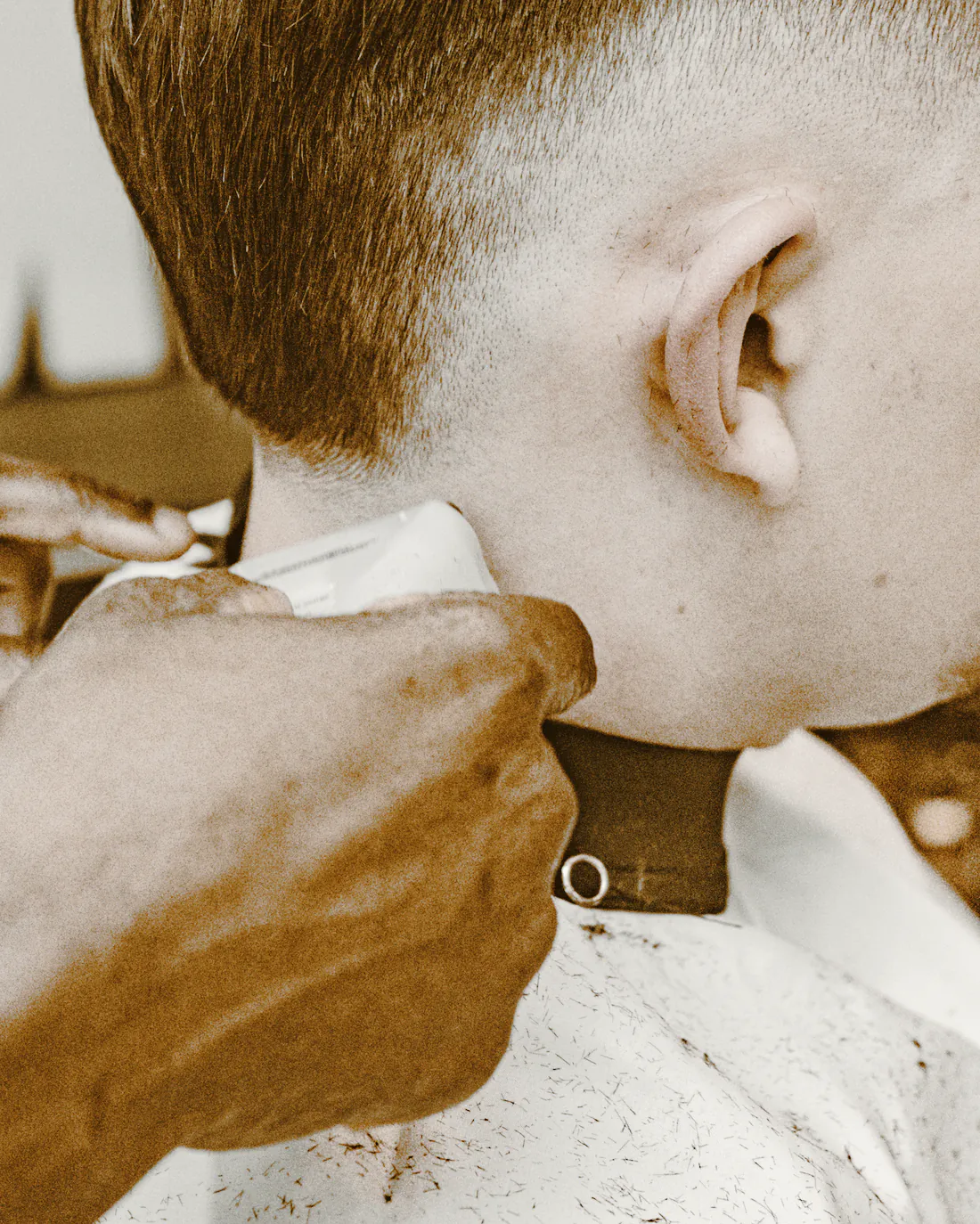 A barber’s hands taking clippers up the back of a client’s skin fade