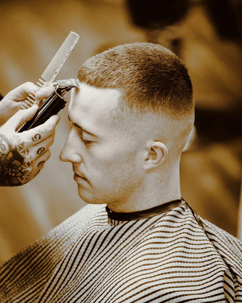 A barber running clippers along a client’s short fade, a comb in the other hand