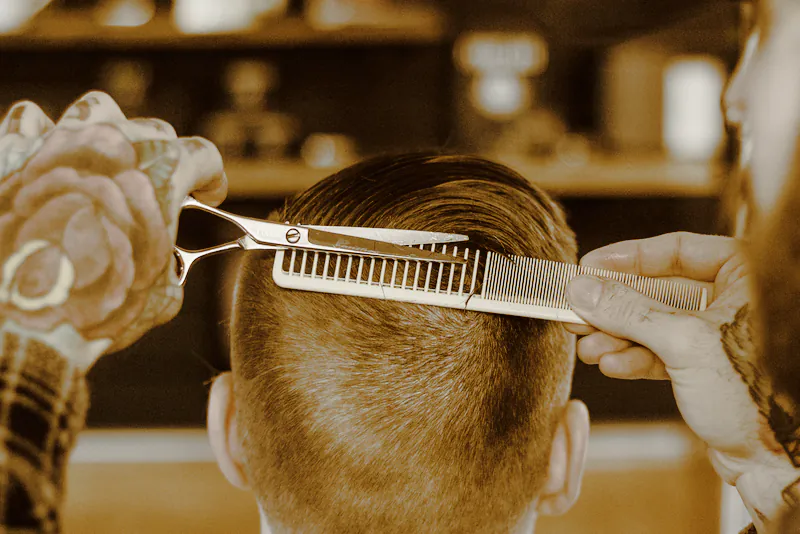 Scissors over a gold comb, taking a short haircut down at the back