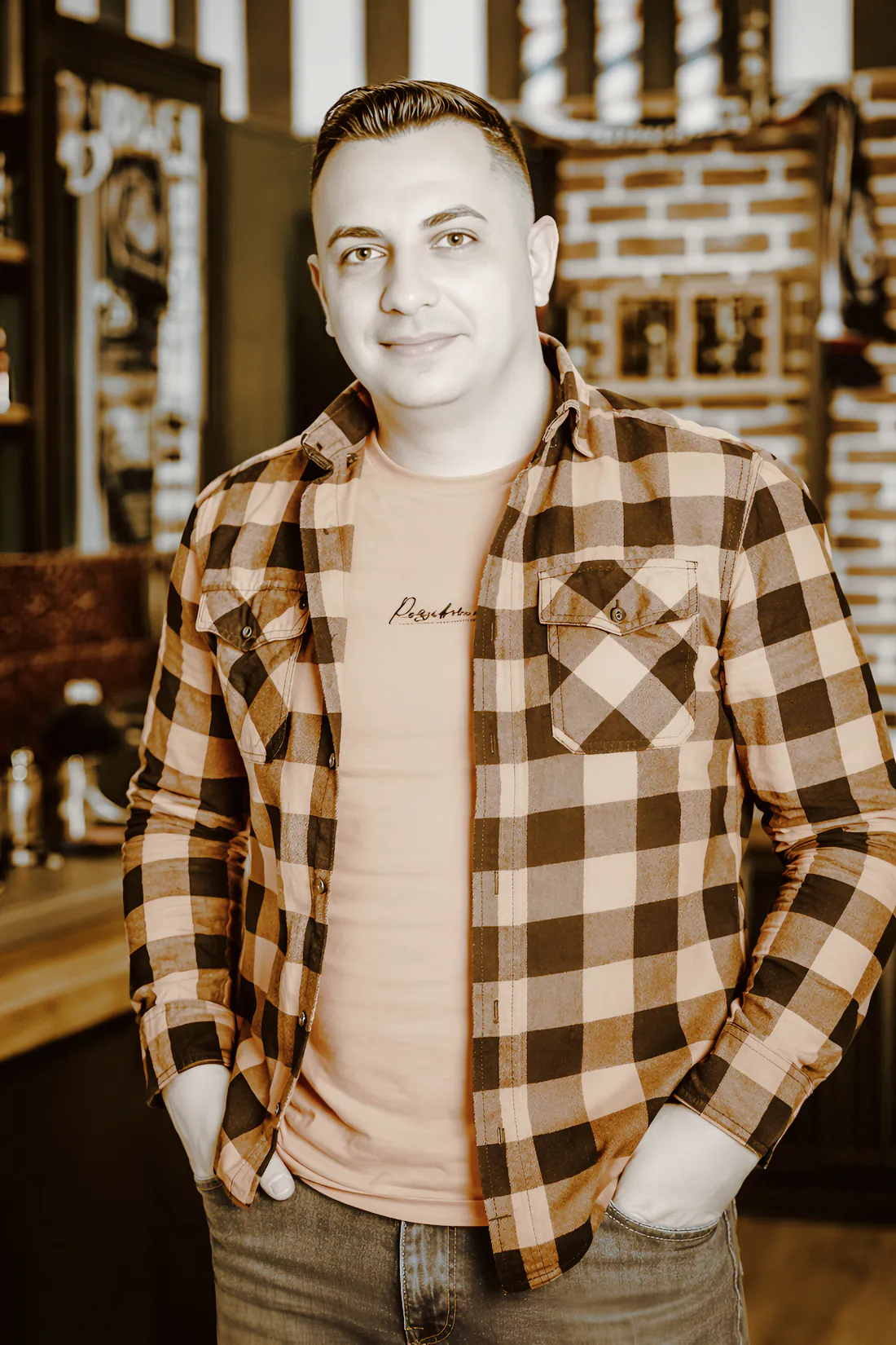 A smiling barber in a checked flannel shirt standing in his shop