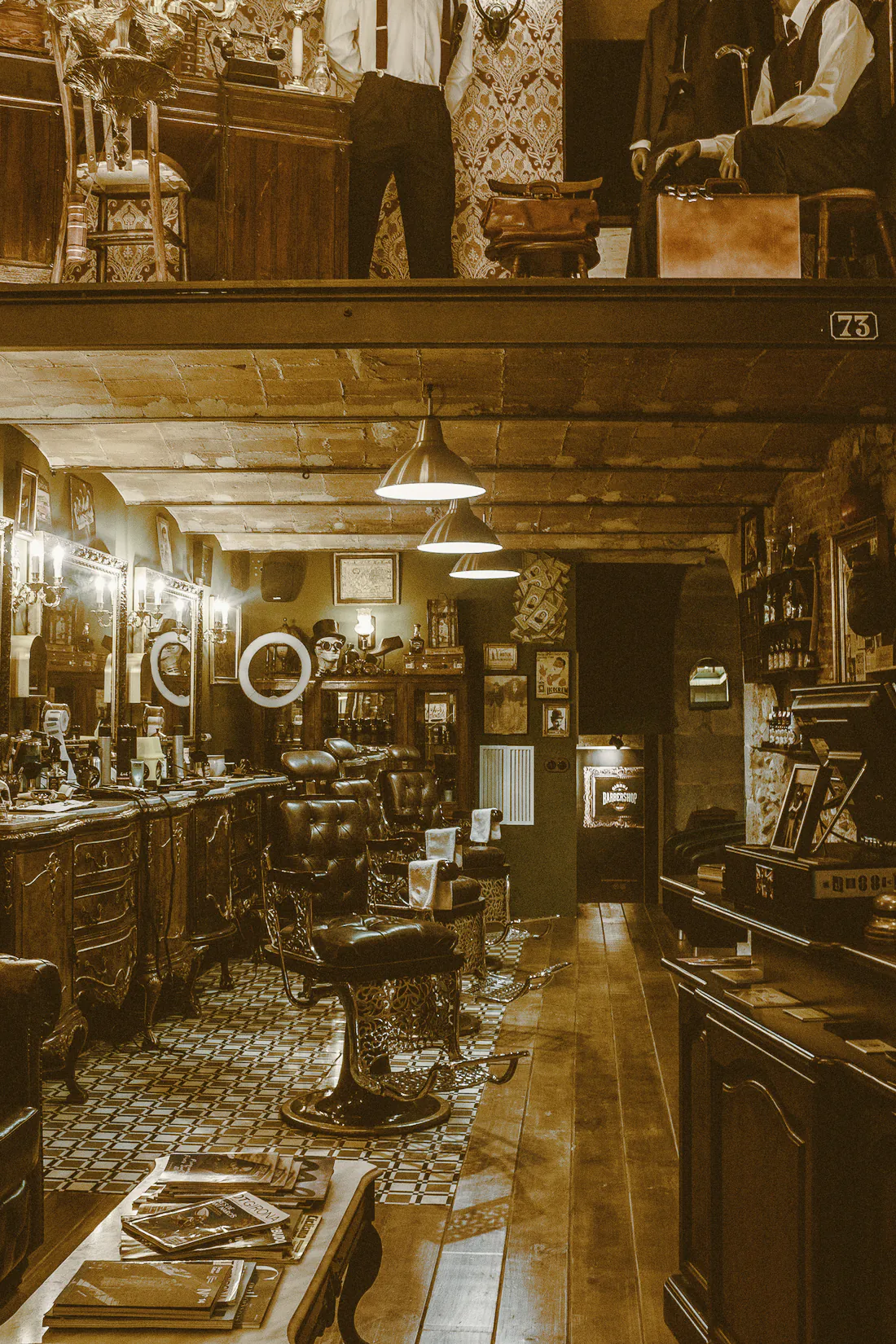 A long, dim barbershop with old chairs, mirrors and hanging lamps