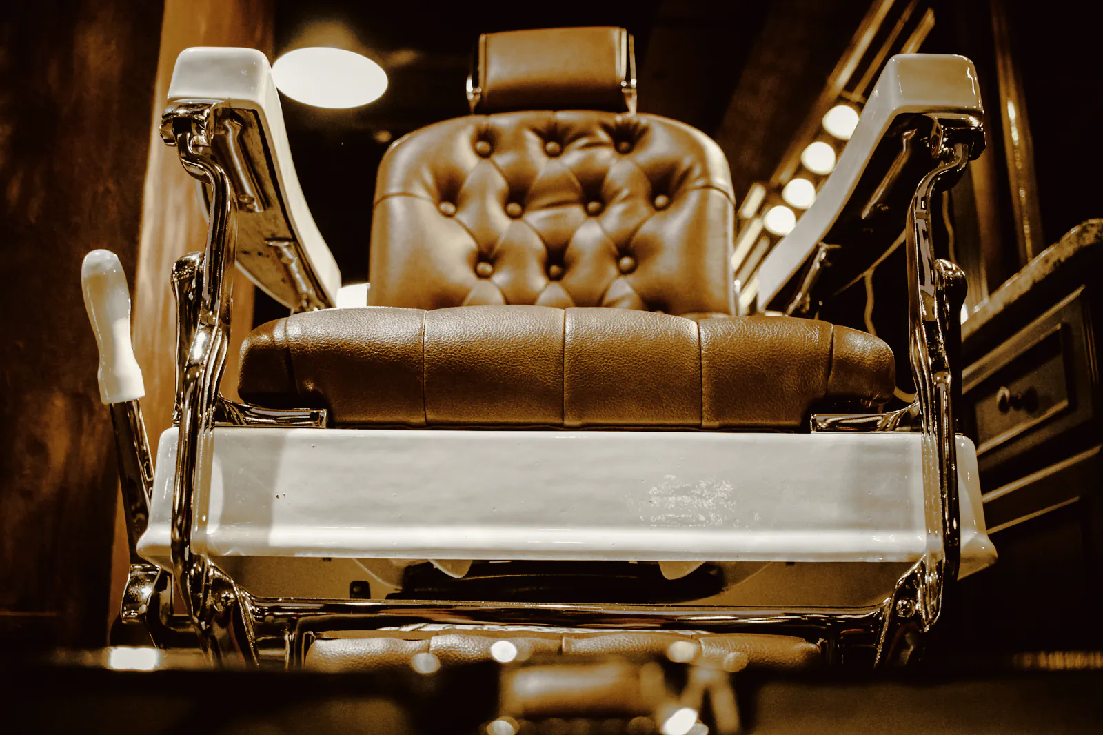 A tufted brown leather barber chair with a chrome footrest under warm lights