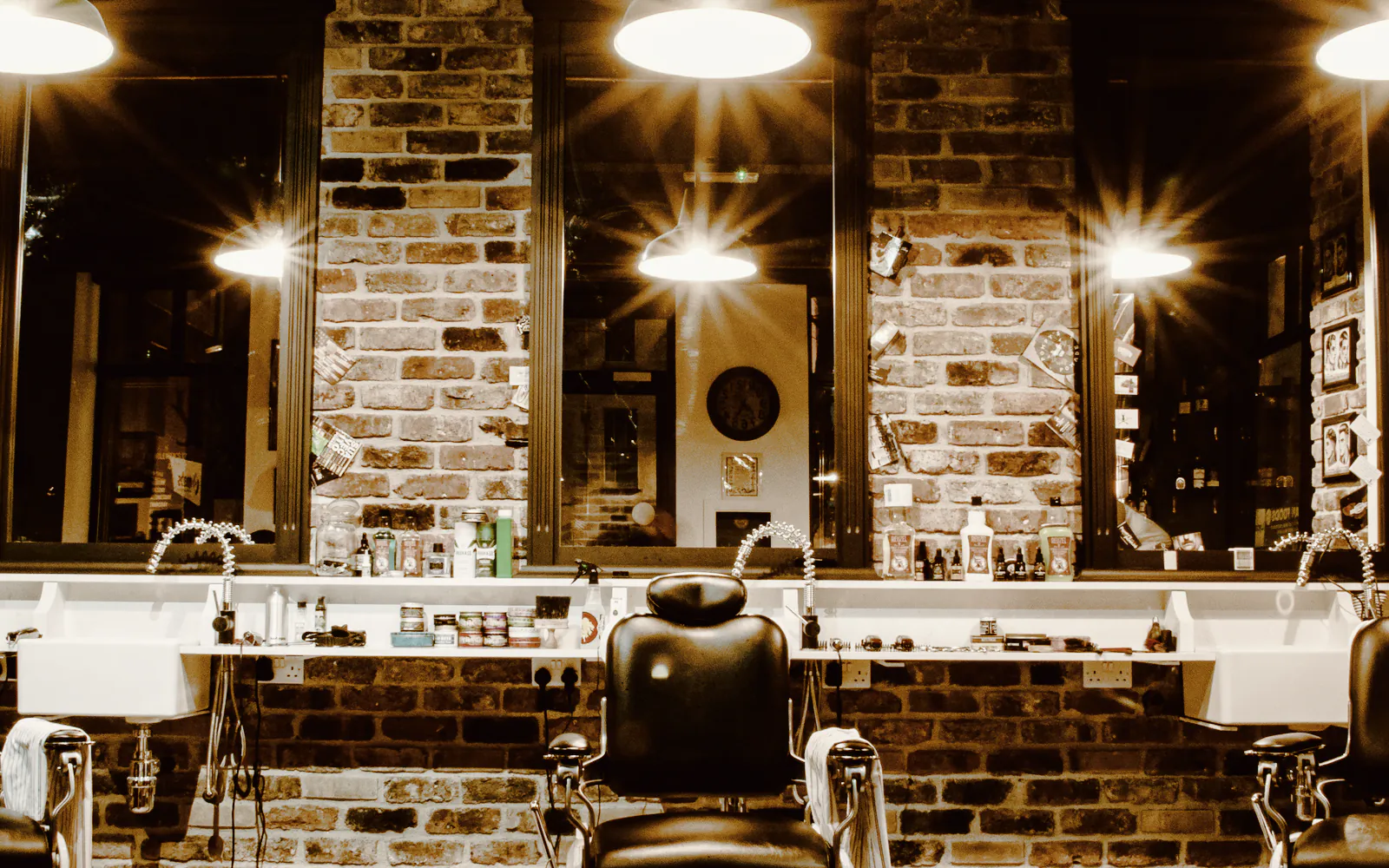 Black leather barber chairs, tall mirrors and pendant lights against a brick wall