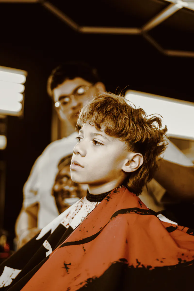 A boy in a red and black cape having his curly hair cut